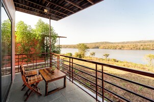 Una mesa y sillas de madera en un balcón con vistas a un lago y árboles.