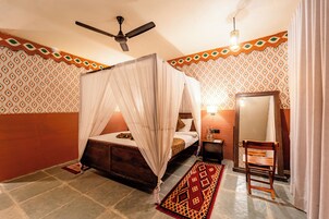 Un dormitorio con una cama con dosel, un ventilador de techo, una mesita de noche con lámpara, un espejo y una silla de madera.