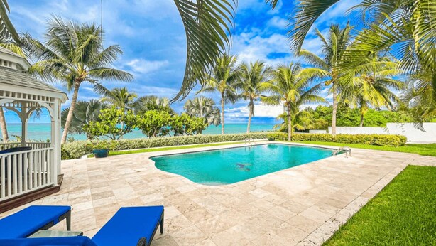Zona de piscina con vista despejada al océano, rodeada de palmeras y un pabellón.