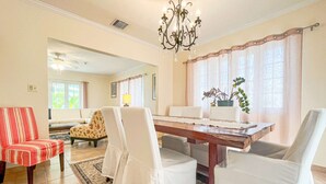 Un comedor con una mesa de madera, sillas blancas y una lámpara de araña.