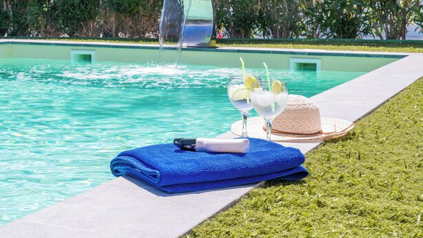 Ein Poolbereich mit blauem Handtuch, einer Flasche und einem Hut auf dem Rasen.