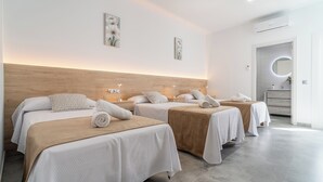 Ein Hotelzimmer mit drei Betten, einem Holzkopfende, einem runden Spiegel und einem kleinen Badezimmer mit Waschbecken und Spiegel.