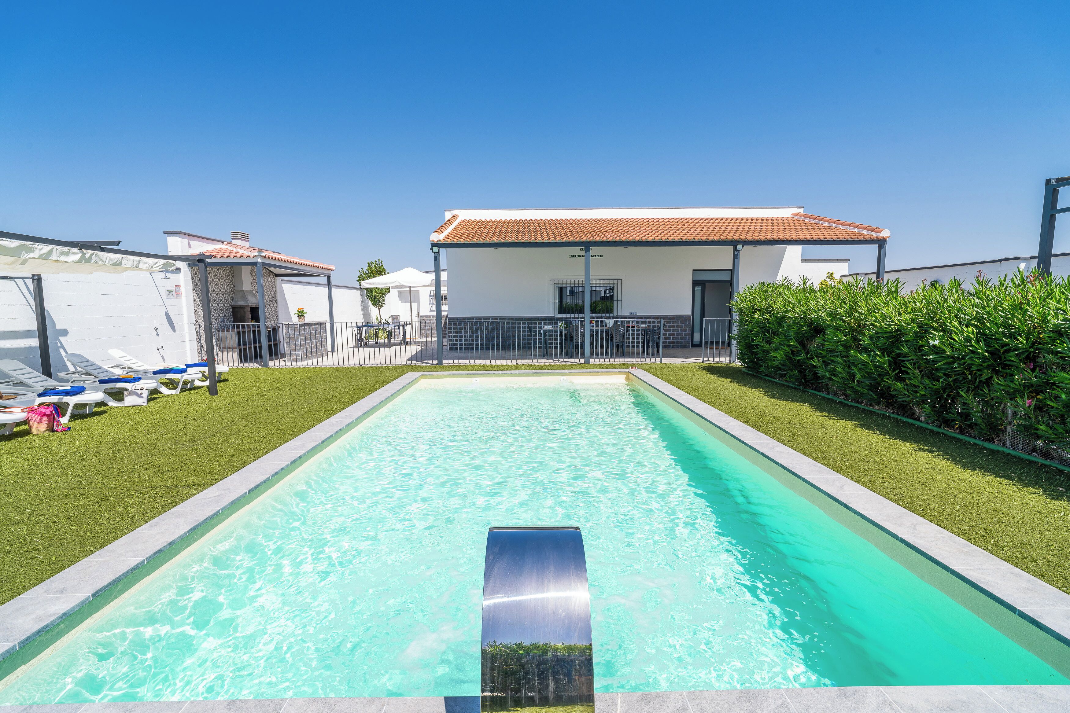 A rectangular swimming pool with clear blue water, surrounded by a well-maintained lawn and a building with a tiled roof.