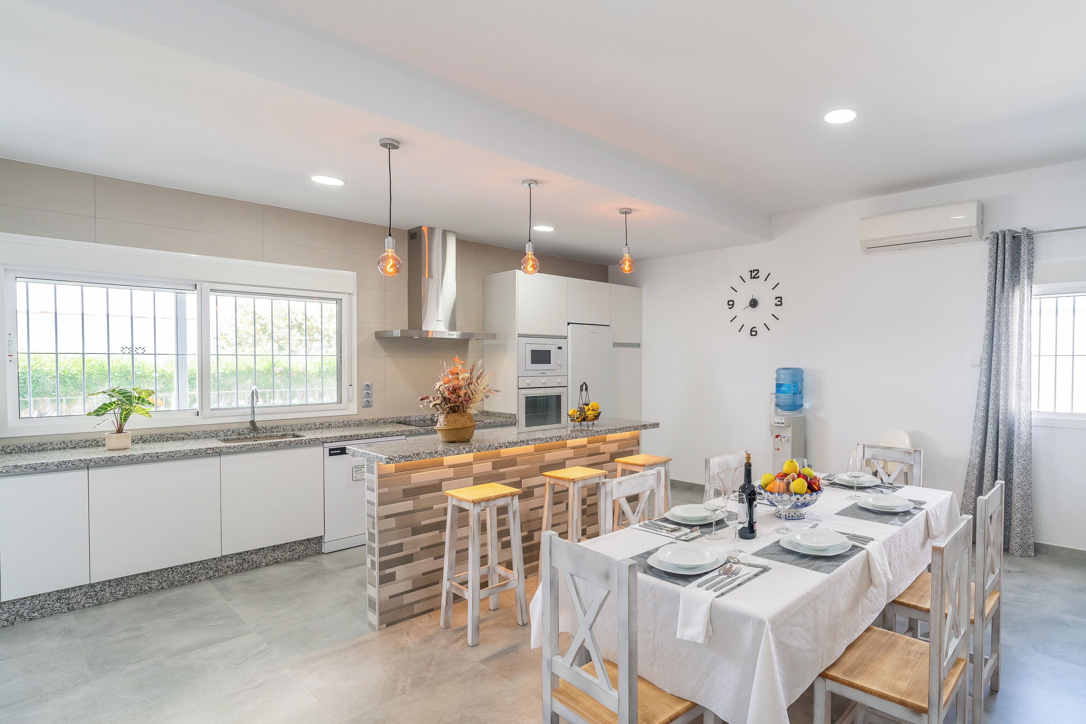 A modern kitchen with a central island, bar stools, and a dining table set for four.