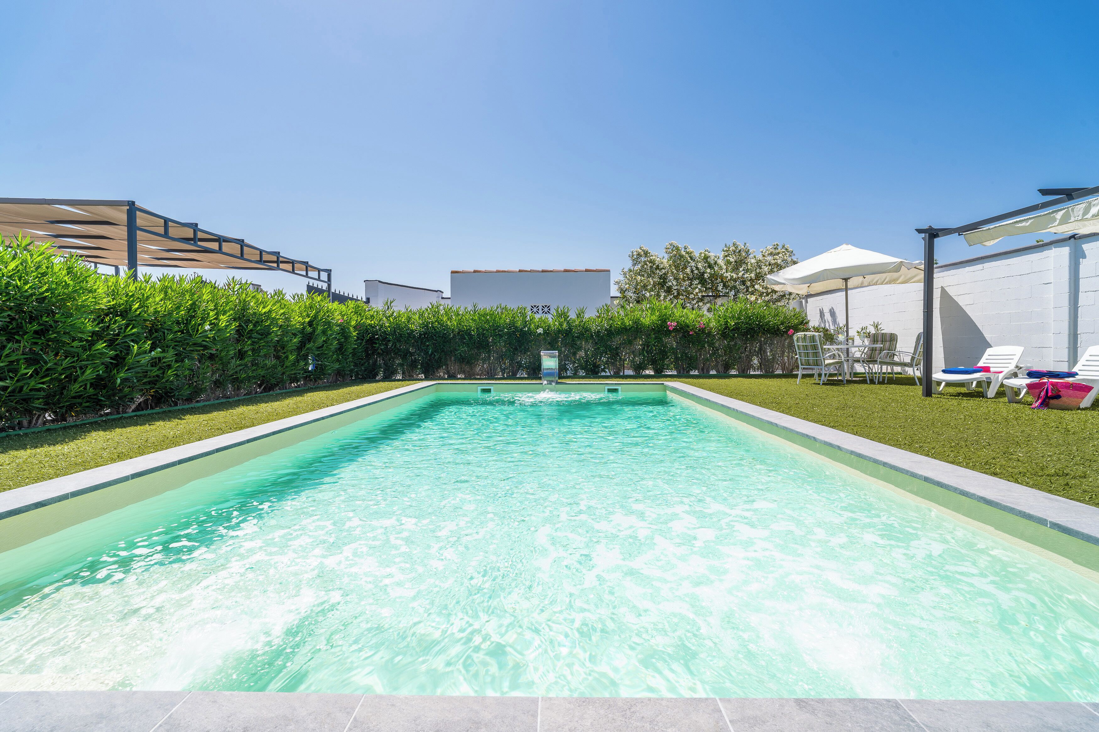 A rectangular swimming pool with a clear blue water surface, surrounded by a well-maintained lawn and a hedge.