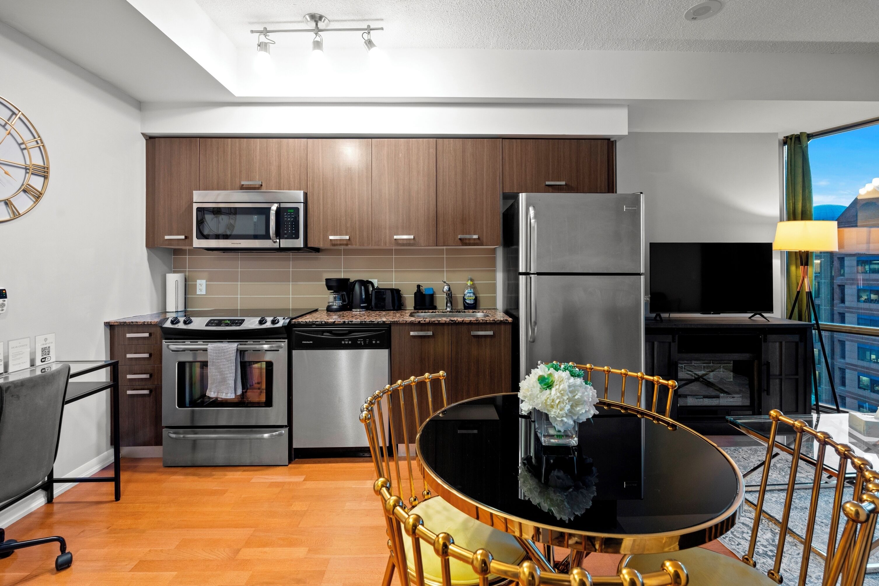 Una cocina moderna con armarios de madera, electrodomésticos de acero inoxidable, una mesa de comedor con sillas y vistas a la ciudad a través de una ventana.