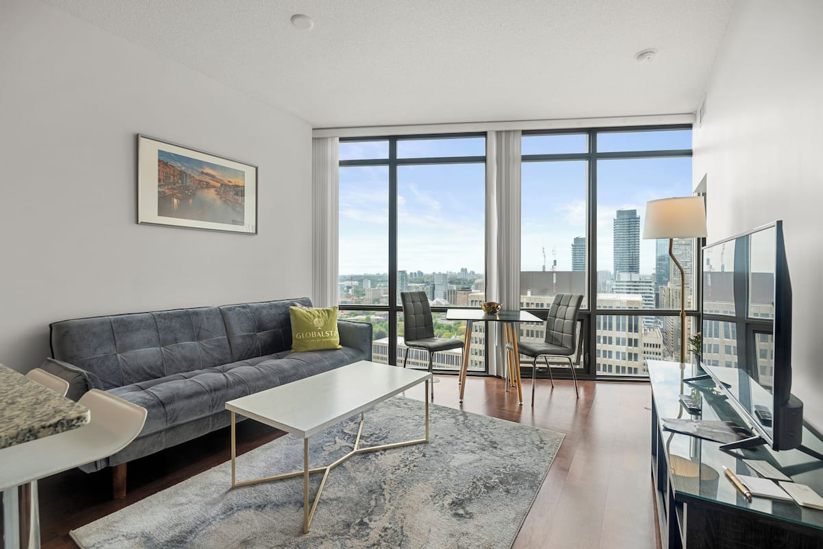 Una sala de estar moderna con un sofá gris, una mesa de centro blanca y vistas a la ciudad a través de amplios ventanales.