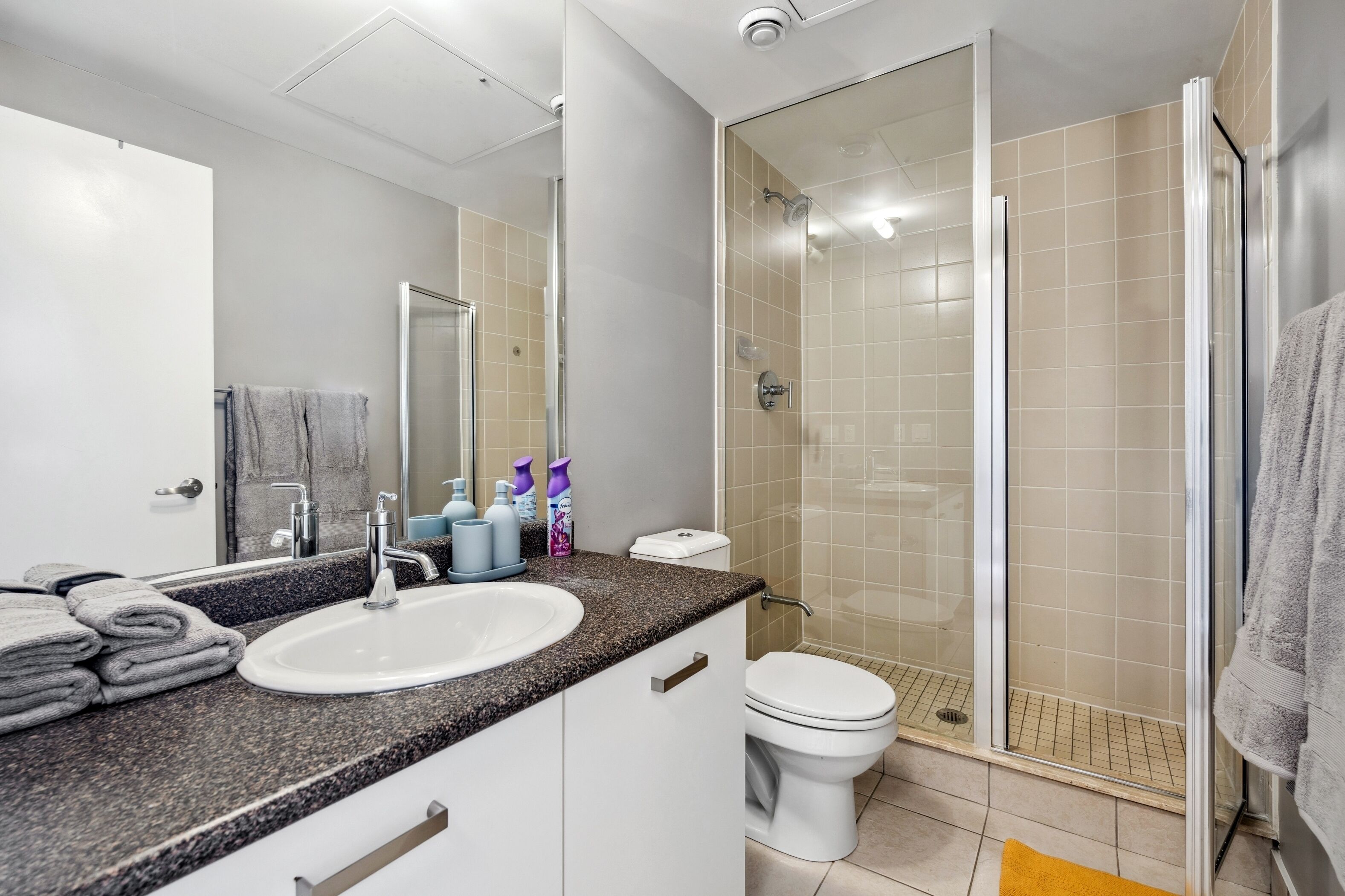 Une salle de bain moderne avec un comptoir en granit, un lavabo blanc, des toilettes et une douche à parois de verre.