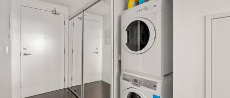 Un lavadero con lavadora y secadora de carga frontal, un espejo y una puerta que da a otra habitación.