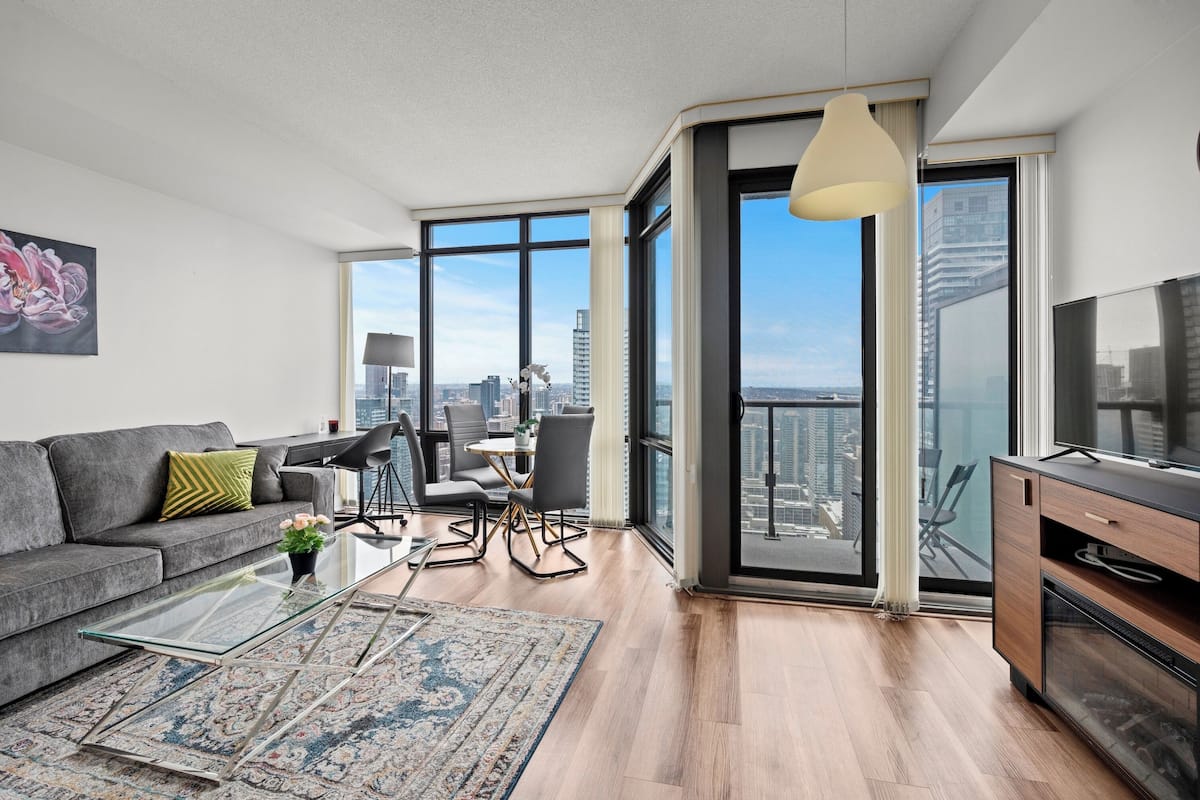 Una sala moderna con sofá, mesa de centro y vistas a la ciudad a través de grandes ventanales.