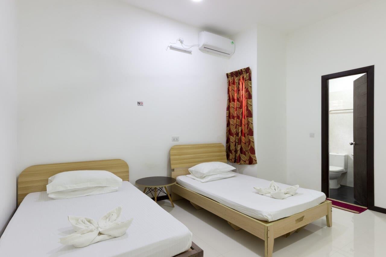 A hotel room with two beds, a small table, an air conditioning unit, a curtain, and a door leading to a bathroom.