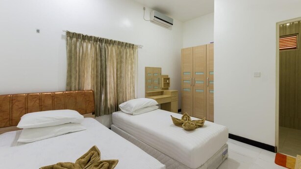 A hotel room with two beds, a wooden headboard, a bathroom with a mirror and towel rack, and a wardrobe with glass doors. - Surf Trip Maldives (Thulusdhoo Island)