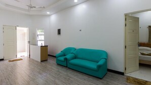A room with a teal sofa, a ceiling fan, a small window, and a door leading to another room. - Surf Trip Maldives (Thulusdhoo Island)