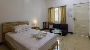 A hotel room with a bed, bedside table, lamp, sofa, and a glass table. - Surf Trip Maldives (Thulusdhoo Island)