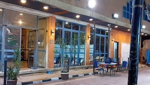 A building with large windows, a tiled patio, and outdoor seating. - New Siesta Hotel  (Alexandria)