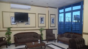 A living room with a TV, framed pictures, and two sofas. - New Siesta Hotel  (Alexandria)