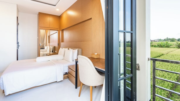 A modern bedroom with a bed, desk, and chair, a large mirror, and a view of a green landscape through an open door. - Asasta Villa by Betterplace (Tabanan)