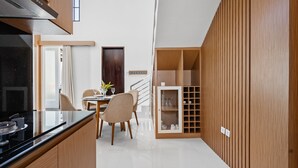 A modern kitchen with a black countertop, wooden cabinets, and a dining area with a table and chairs. - Asasta Villa by Betterplace (Tabanan)