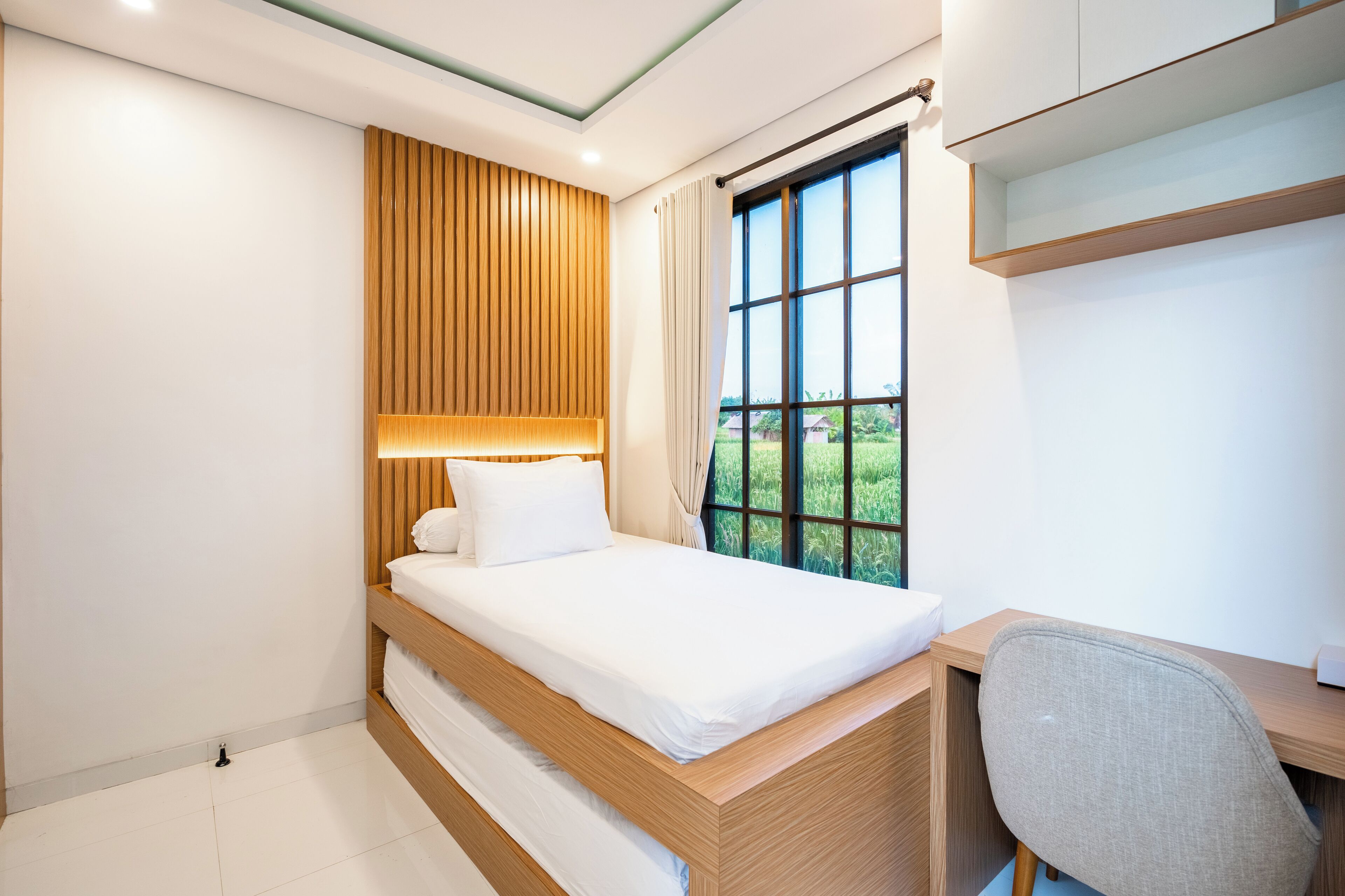 Une chambre moderne avec une tête de lit en bois, une grande fenêtre avec des rideaux, un bureau avec une chaise et un lit superposé.