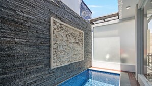 A modern pool area with a stone wall and a decorative relief. - Asasta Villa by Betterplace (Tabanan)