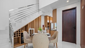 A modern dining area with a glass staircase, wooden paneling, and a wooden door. - Asasta Villa by Betterplace (Tabanan)