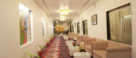 A hotel corridor with a red carpet, sofas, potted plants, and artwork on the walls.