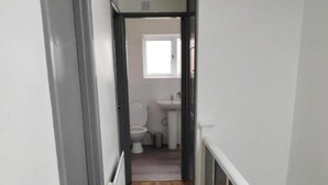 Ein schmaler Flur mit Holzboden, der zu einem Badezimmer mit Toilette und Waschbecken führt.