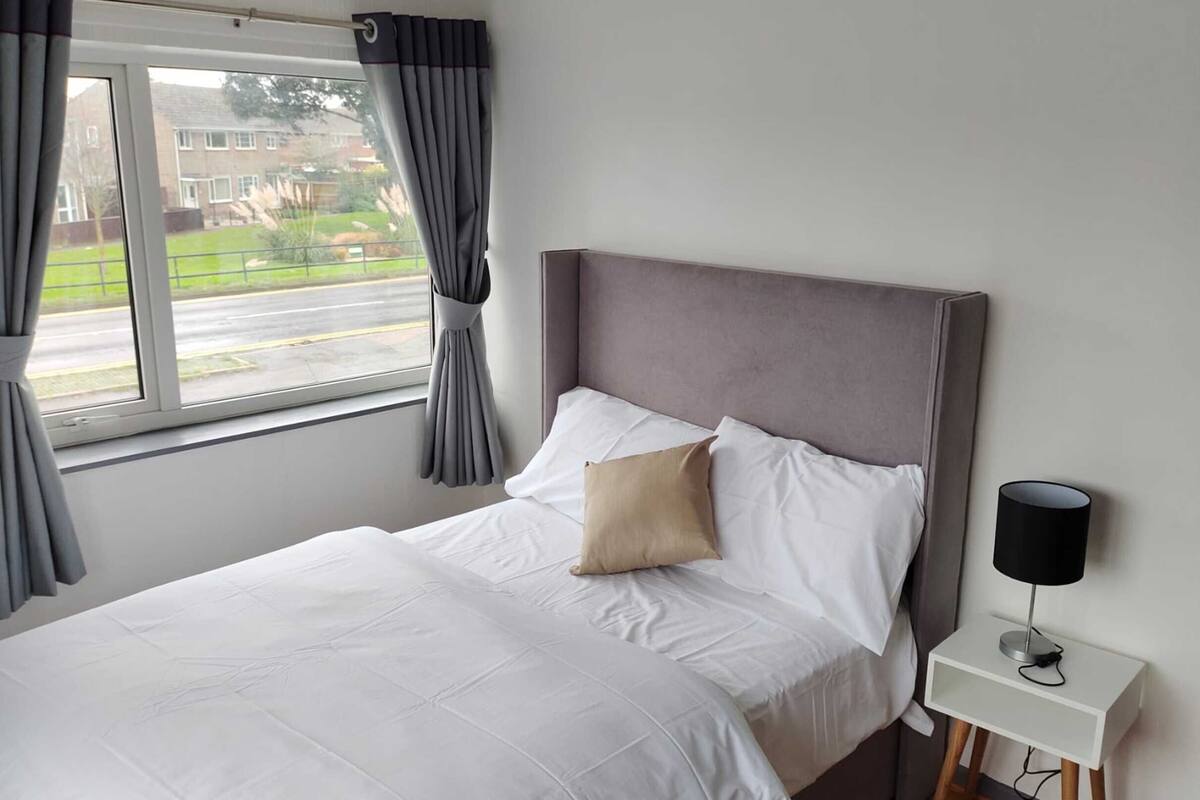 Ein Hotelzimmer mit einem Bett, einem Nachttisch, einer Lampe und einem Fenster mit Vorhängen.