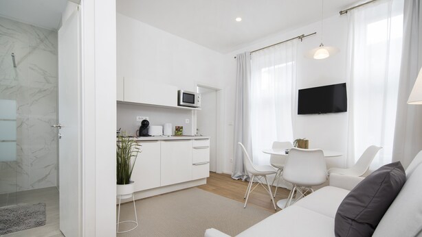 Una sala de estar moderna y bien iluminada, con un sofá, un comedor con mesa y sillas, y una cocina con microondas y armarios.