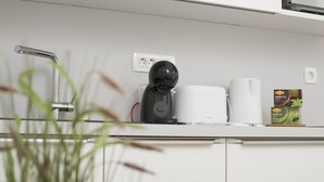 Cocina moderna con cafetera, hervidor y una caja de cápsulas de café sobre la encimera.