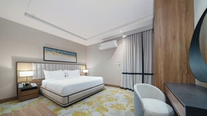 Una habitación de hotel con cama, escritorio, silla, mesita de noche y aire acondicionado.