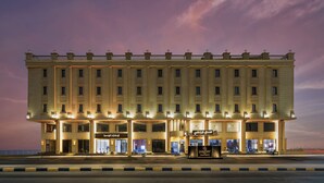 Un hotel grande de varios pisos con una fachada simétrica, múltiples balcones y señalización iluminada.