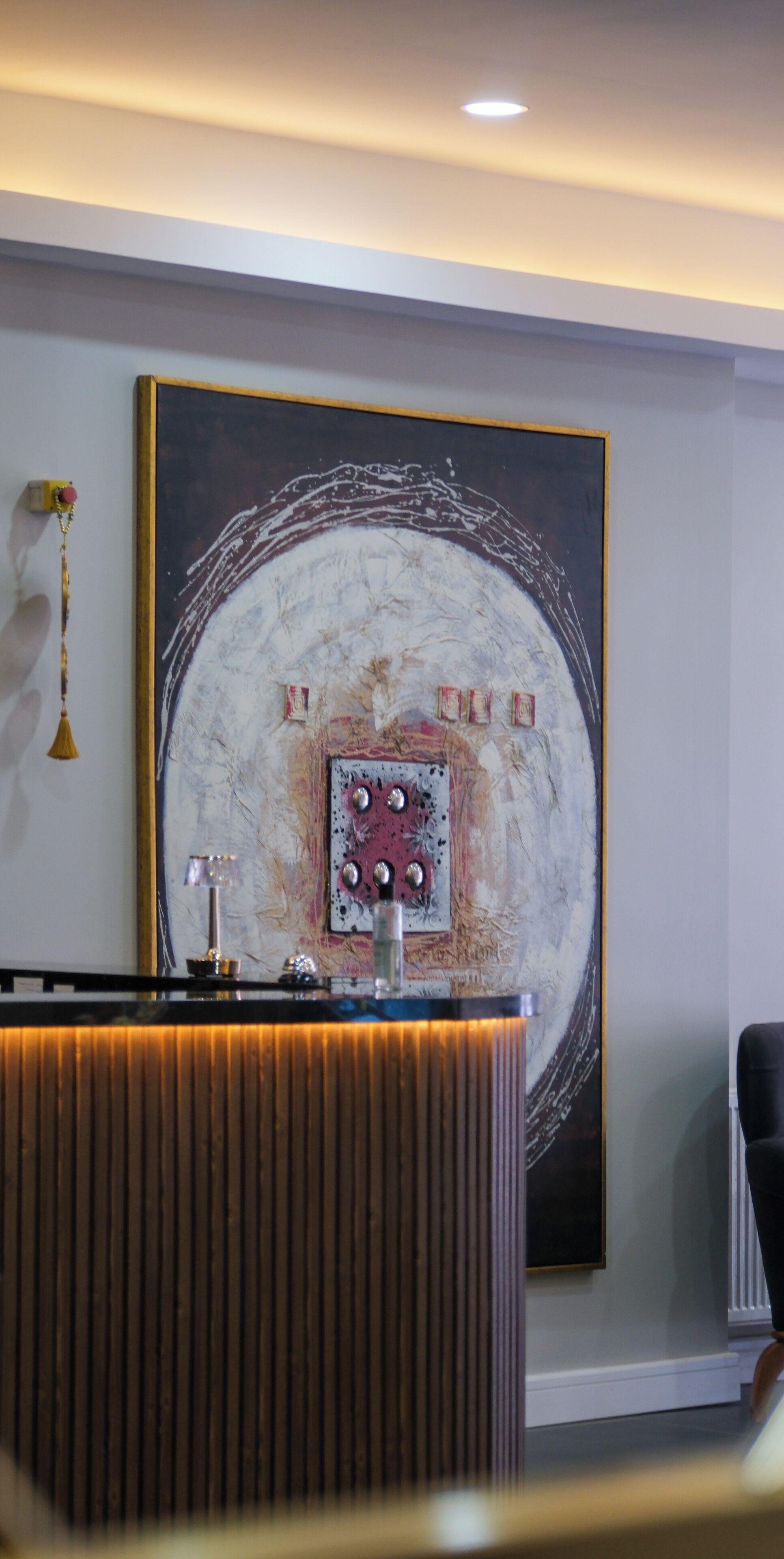 A reception desk with a modern design, a large abstract painting on the wall, and a hanging light fixture.