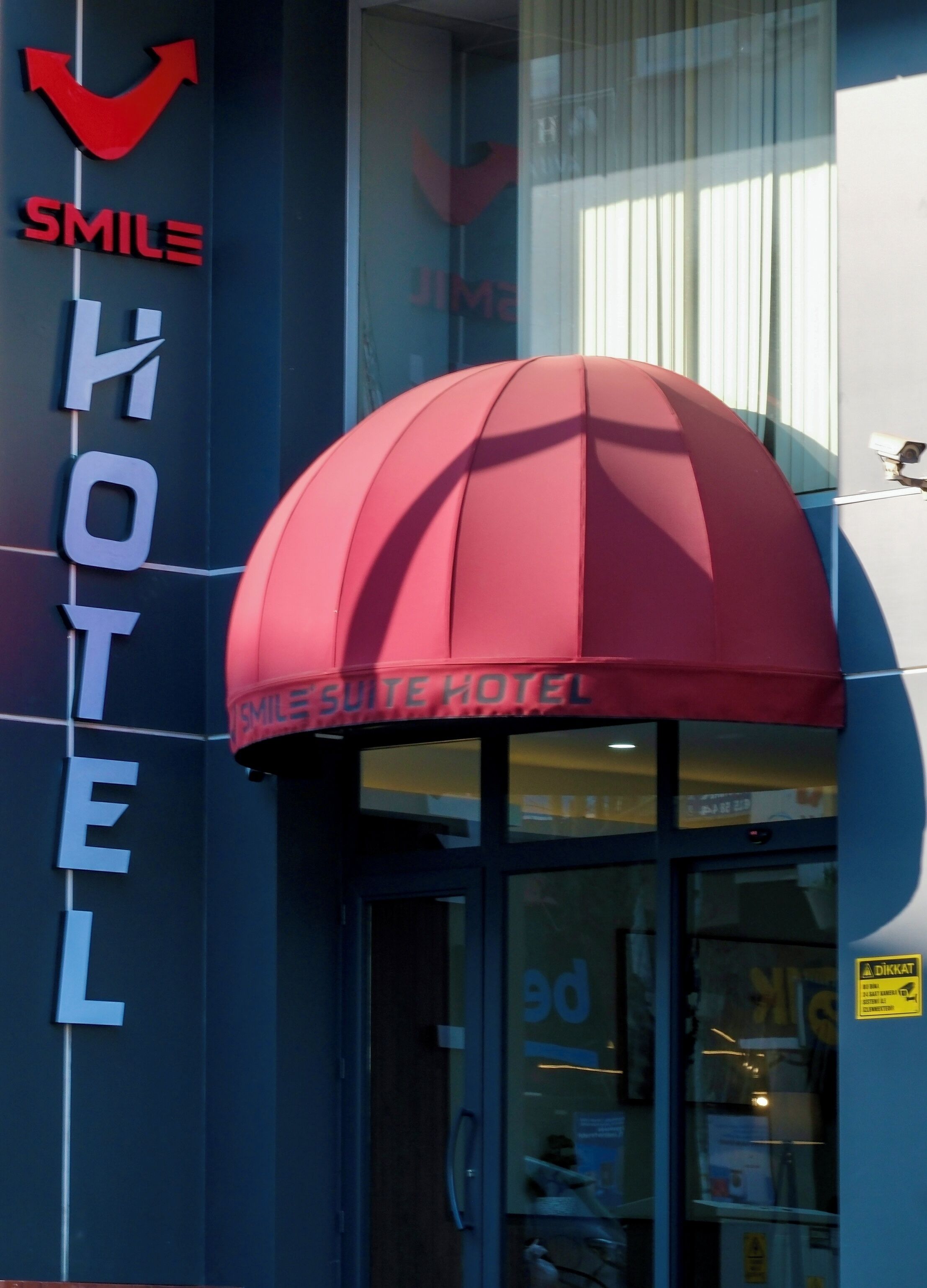 Entrada de un hotel con toldo rojo, un letrero que dice 'SMILE' y un letrero que dice 'HOTEL' en la fachada del edificio.