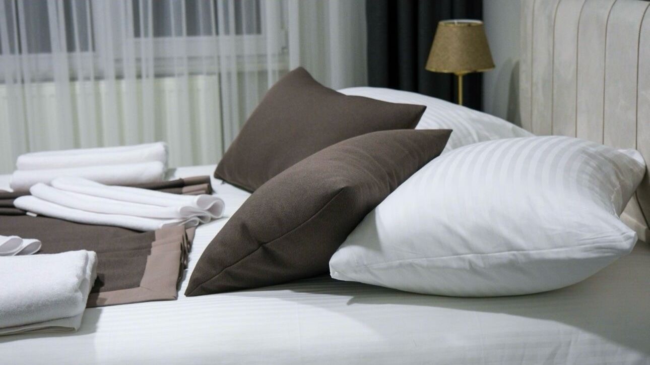 Una cama bien hecha con almohadas blancas y marrones, una colcha blanca y toallas dobladas.