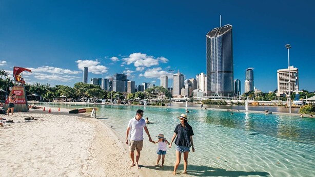A beach with a city skyline in the background, clear blue water, and a lifeguard stand.