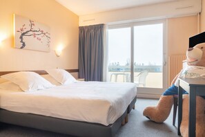 Ein Hotelzimmer mit Bett, einem großen Fenster mit Blick, einem Teddybären und einem Bild an der Wand.