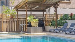 Ett poolområde med solstolar, en pergola och krukväxter.