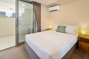A hotel room with a bed, a nightstand, a wall-mounted air conditioner, and a sliding glass door leading to a balcony.