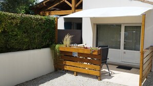 Ein kleiner, abgeschlossener Außenbereich mit einer Holzbank und einem Blumenkasten, einer weißen Markise sowie einer Schiebetür aus Glas.