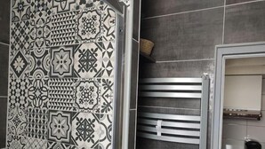 Ein Badezimmer mit gemusterten Fliesen, einer Duschkabine mit Metallrahmen und einer gefliesten Wand.