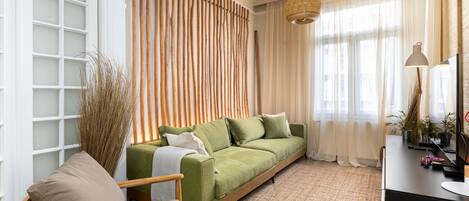 Un salon avec un canapé vert, une chaise en bois et un tapis tissé.