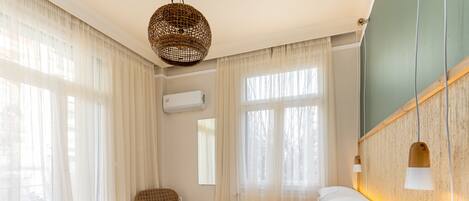 A bedroom with a bed, white curtains, a wicker lamp, and a wooden headboard.