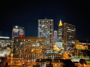 A modern cityscape at night with illuminated buildings, including a prominent skyscraper with a unique triangular top. - Beautiful 14th Floor Condo w Private Balcony Views (Atlanta)