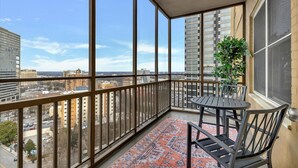 En balkon med et bord og stole, store vinduer og udsigt over bybilledet.