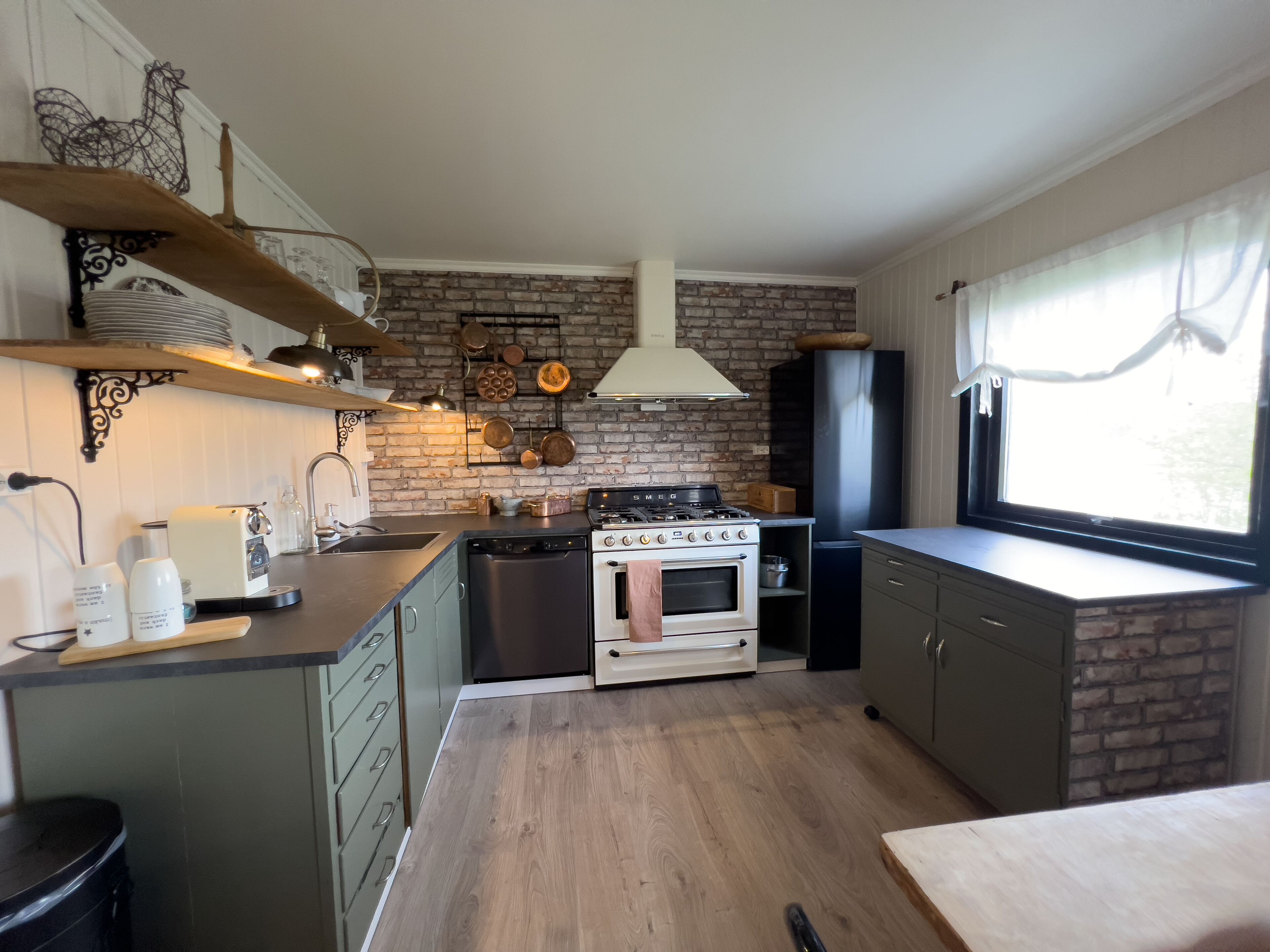 Een kleine keuken met een betegelde bakstenen muur, een inbouwfornuis en een raam met gordijnen.