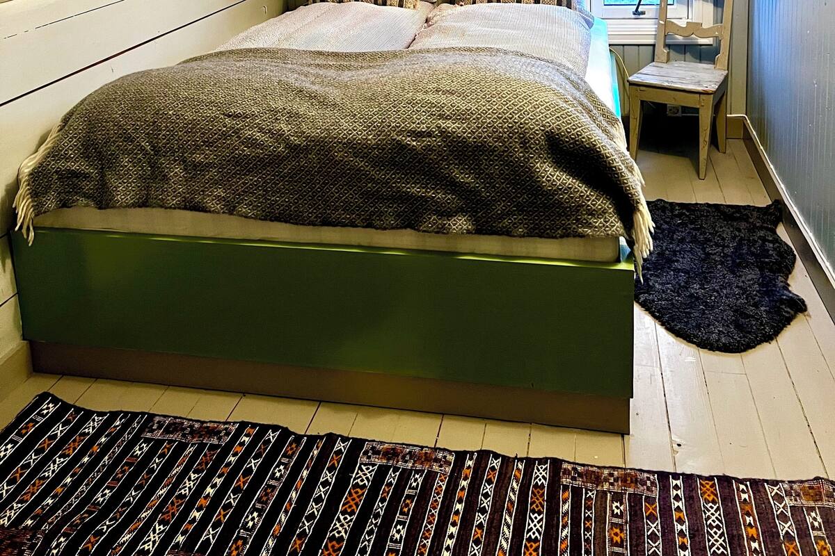 A bedroom with a sloped ceiling, a bed with patterned bedding, a small table with a chair, and a view of the outdoors through a window.