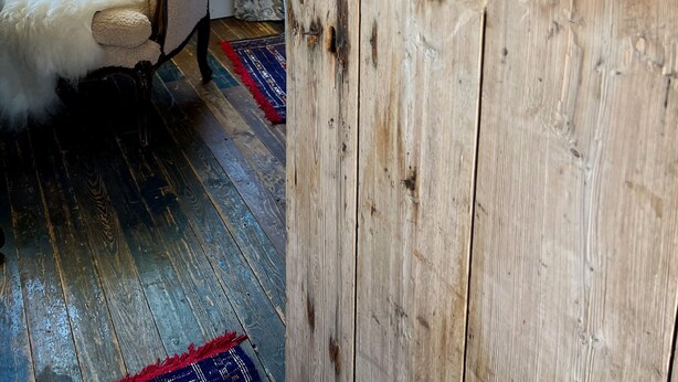 Een rustiek interieur met een houten wand, een zachte fauteuil en een houten vloer.