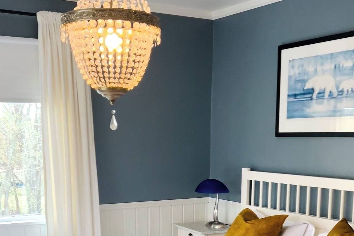 A bedroom with a white bed, a chandelier, a nightstand, and a window with curtains.