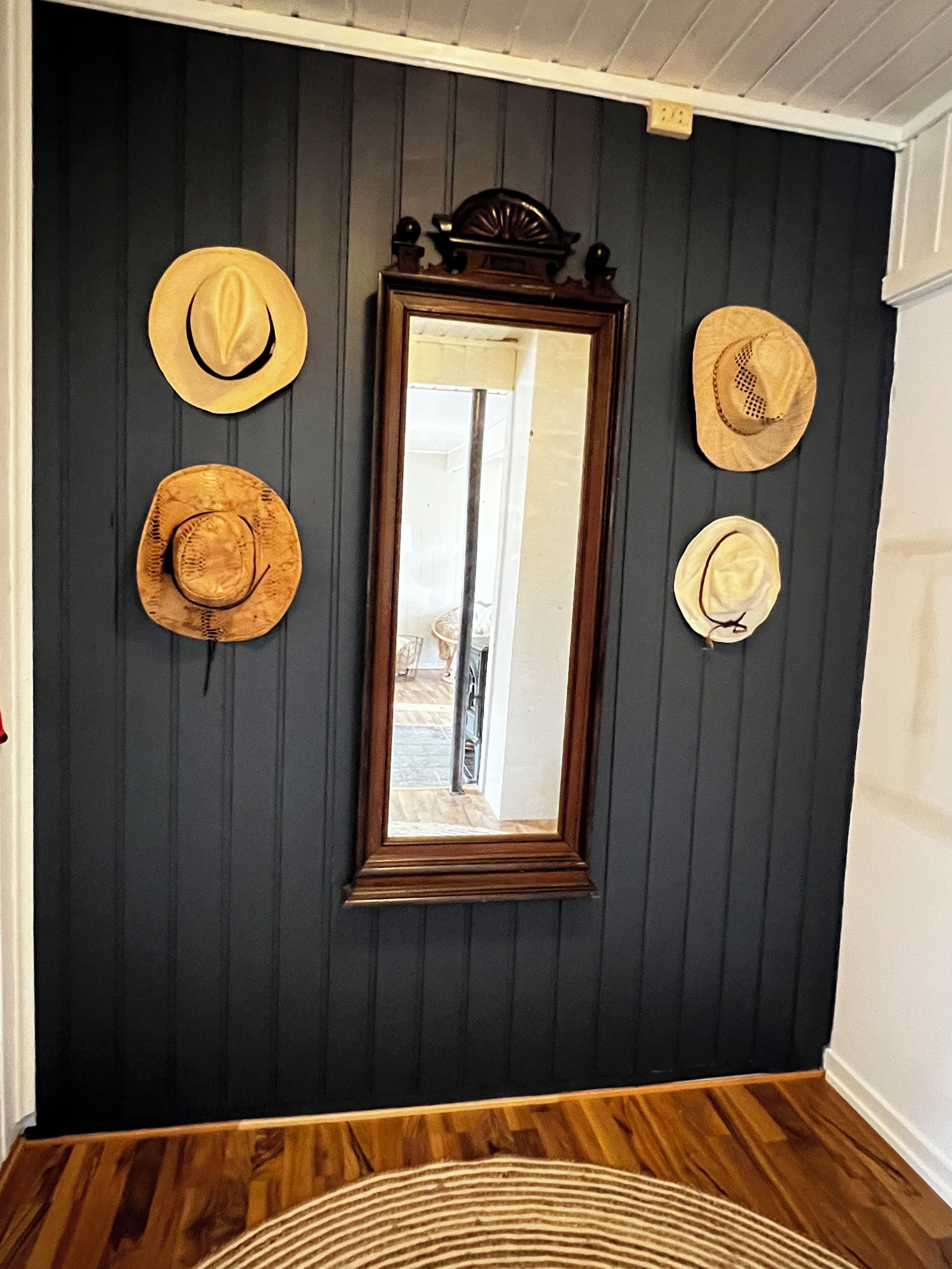 Ein Zimmer mit dunklen Holzwänden, einem Spiegel und vier Hüten, die an der Wand hängen.